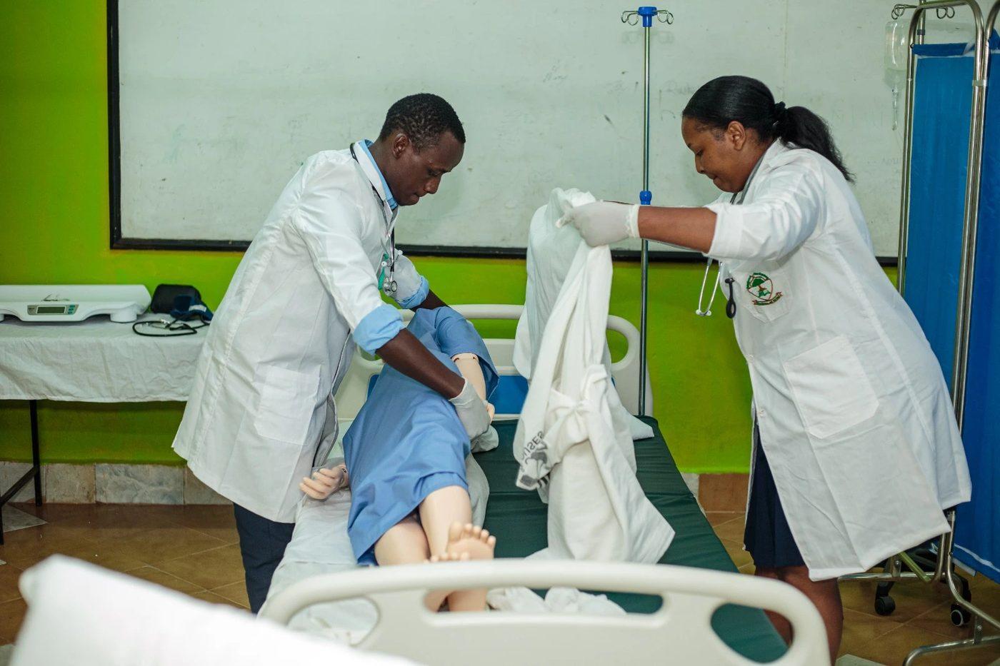 Students in white coats practising at a hospital bed with an IV stand