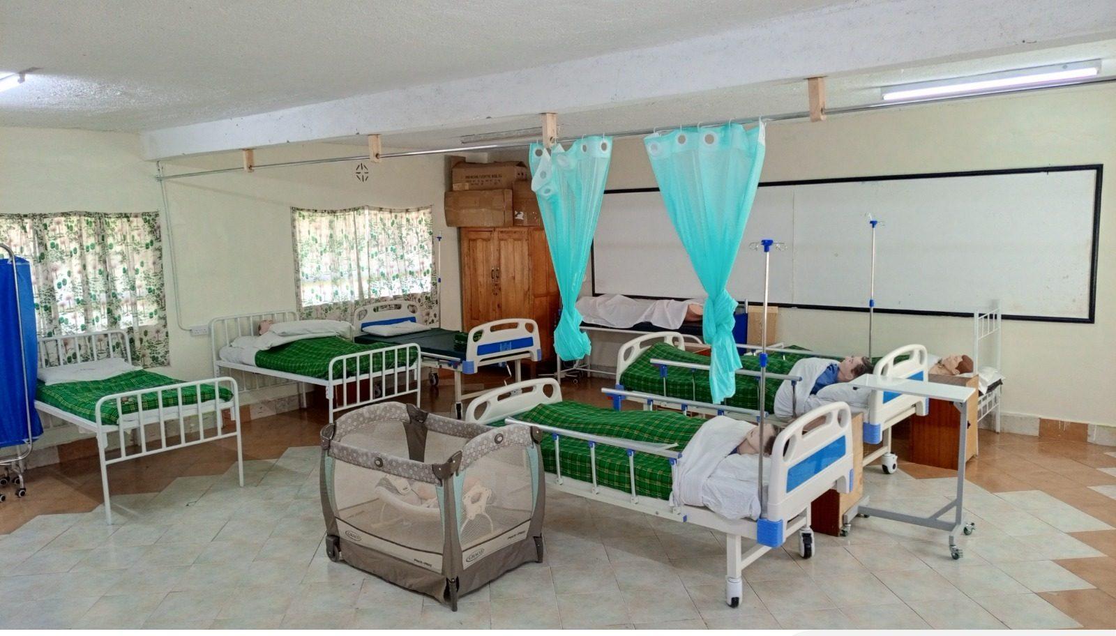 The practice ward: rows of hospital beds with training manikins, drip stands and a cot